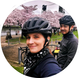 Headshot of a white woman wearing a black bike helmet. A man stands next to her.