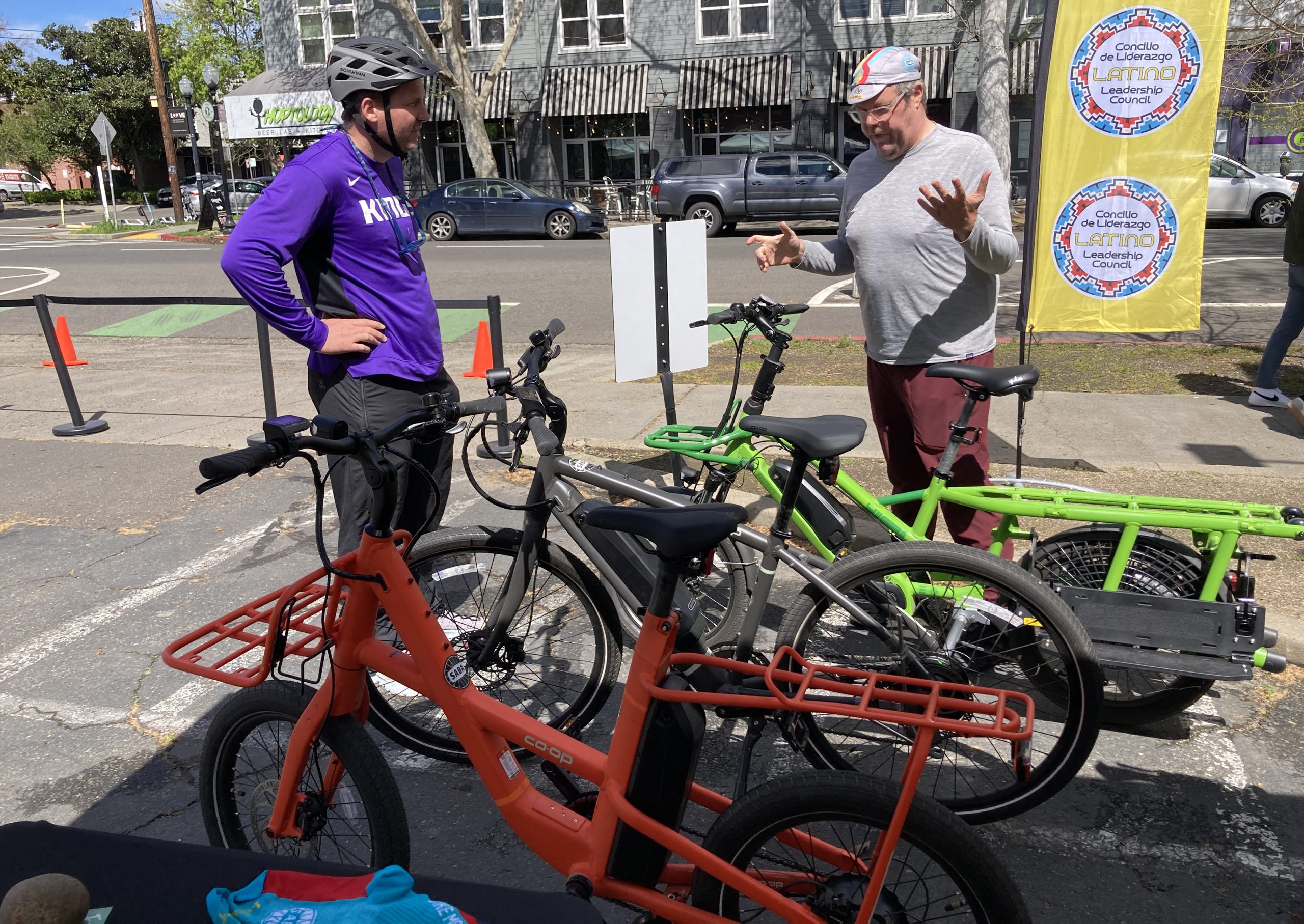 Two men look at e-bikes outside in a parking lot.