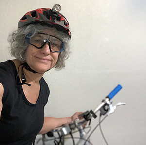 A white woman wearing a red bike helmet holds on to a bike.