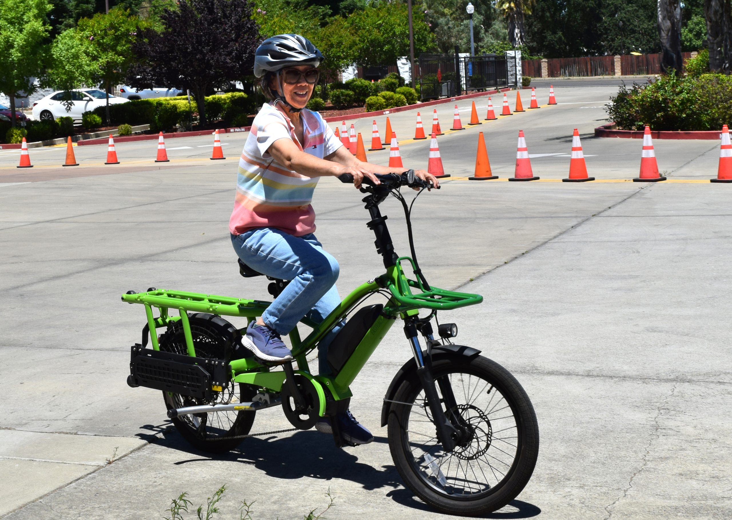 A person wearing a bike helent sits on a green e-bike in a parking lot.