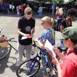 A young man writes in a notebook while a woman watches. There are several bikes.