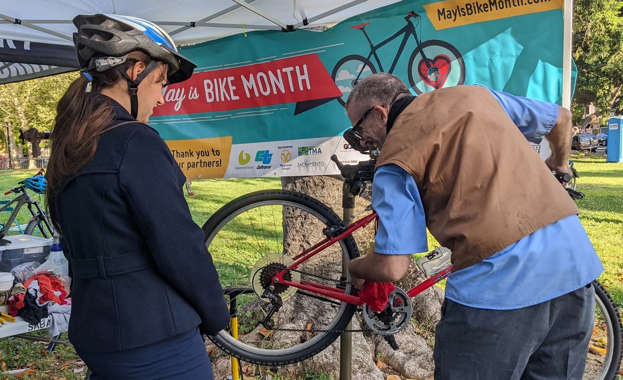 A man works on a bike while a woman wearing a bike helmet watches.