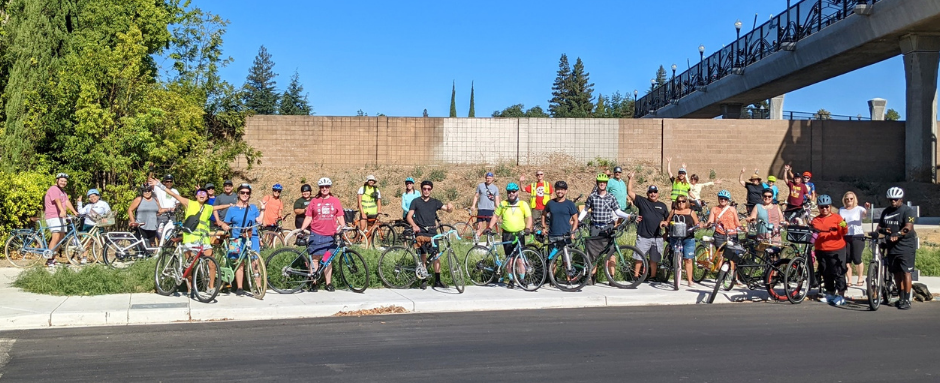 A large group of cyclists by a wall and a bridge.