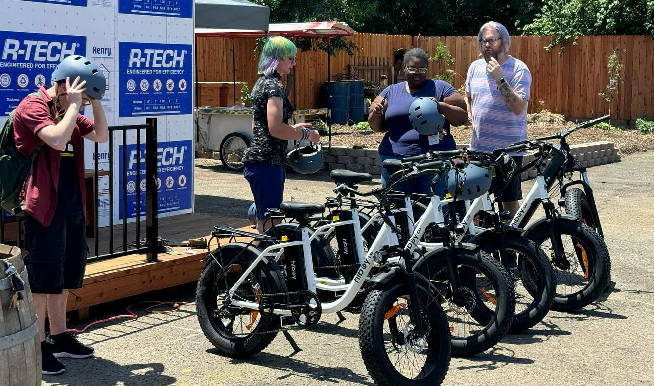 Four people, 3 holding bike helmets, stand next to a row of e-bikes.