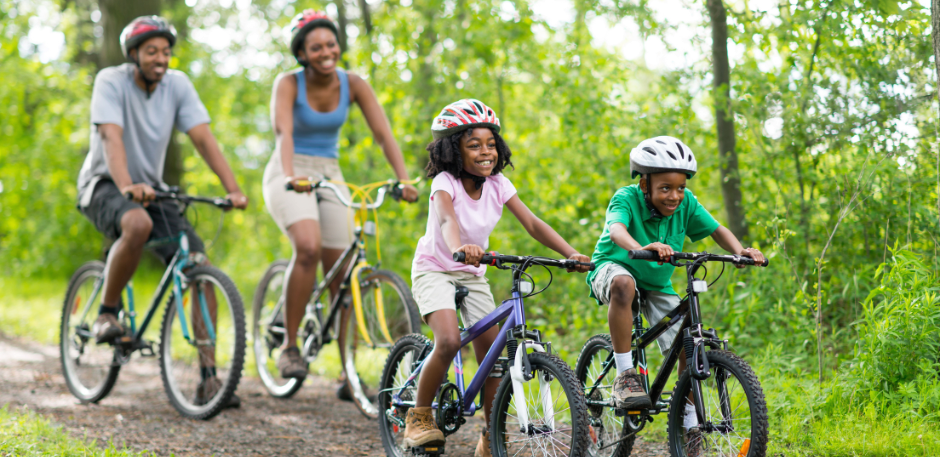 Two adults and two children bike on a dirt path in the woods.