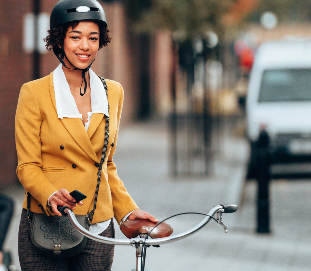 A Black woman wearing a helmet stands next to a bike.