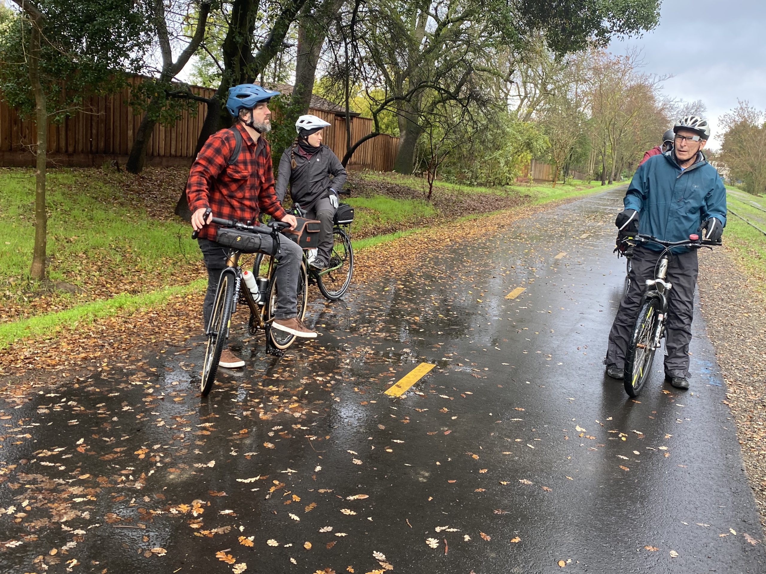 Three cyclists stopped on a wet trail.