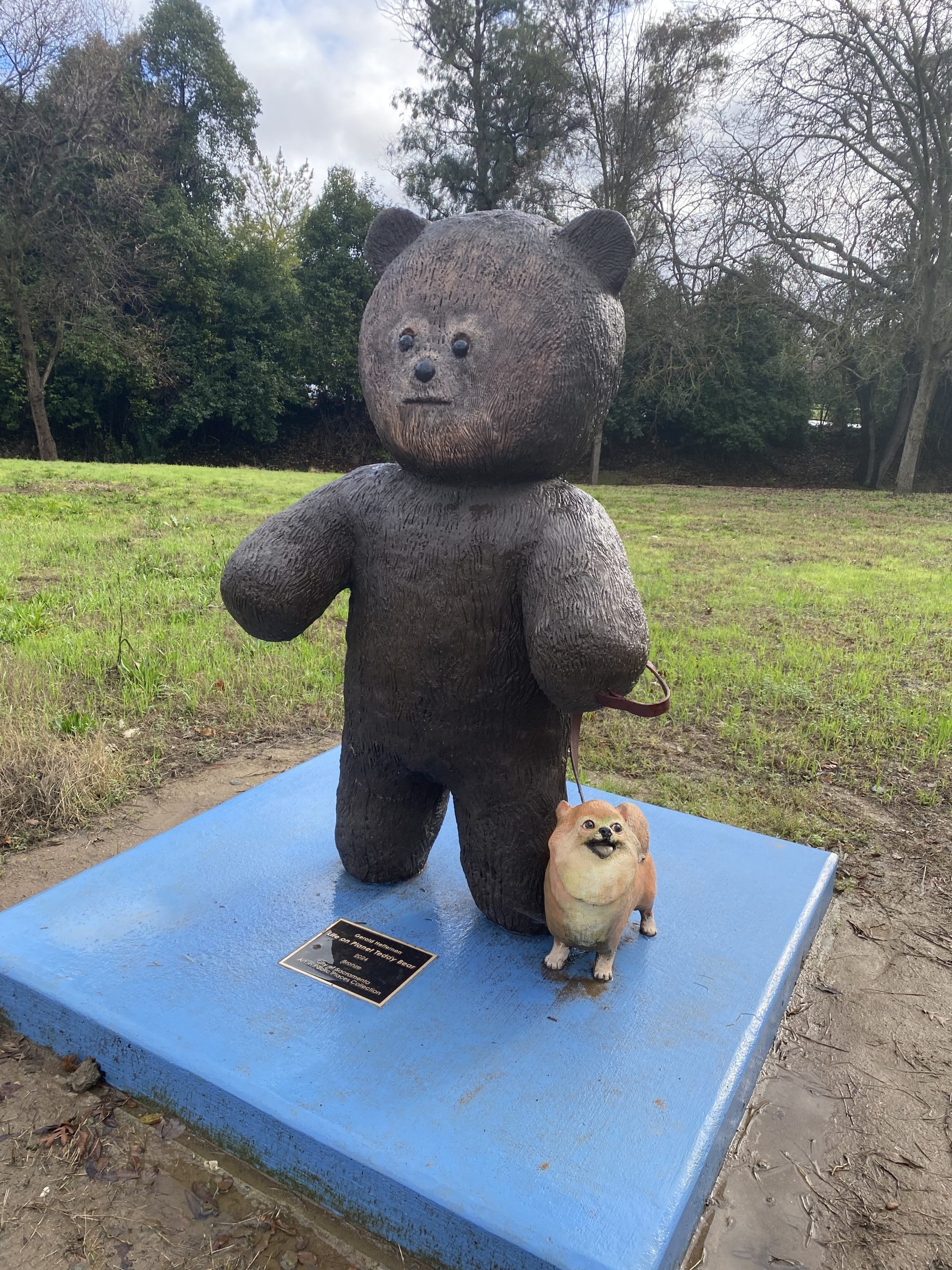 A large teddy bear with a small dog on a leash.