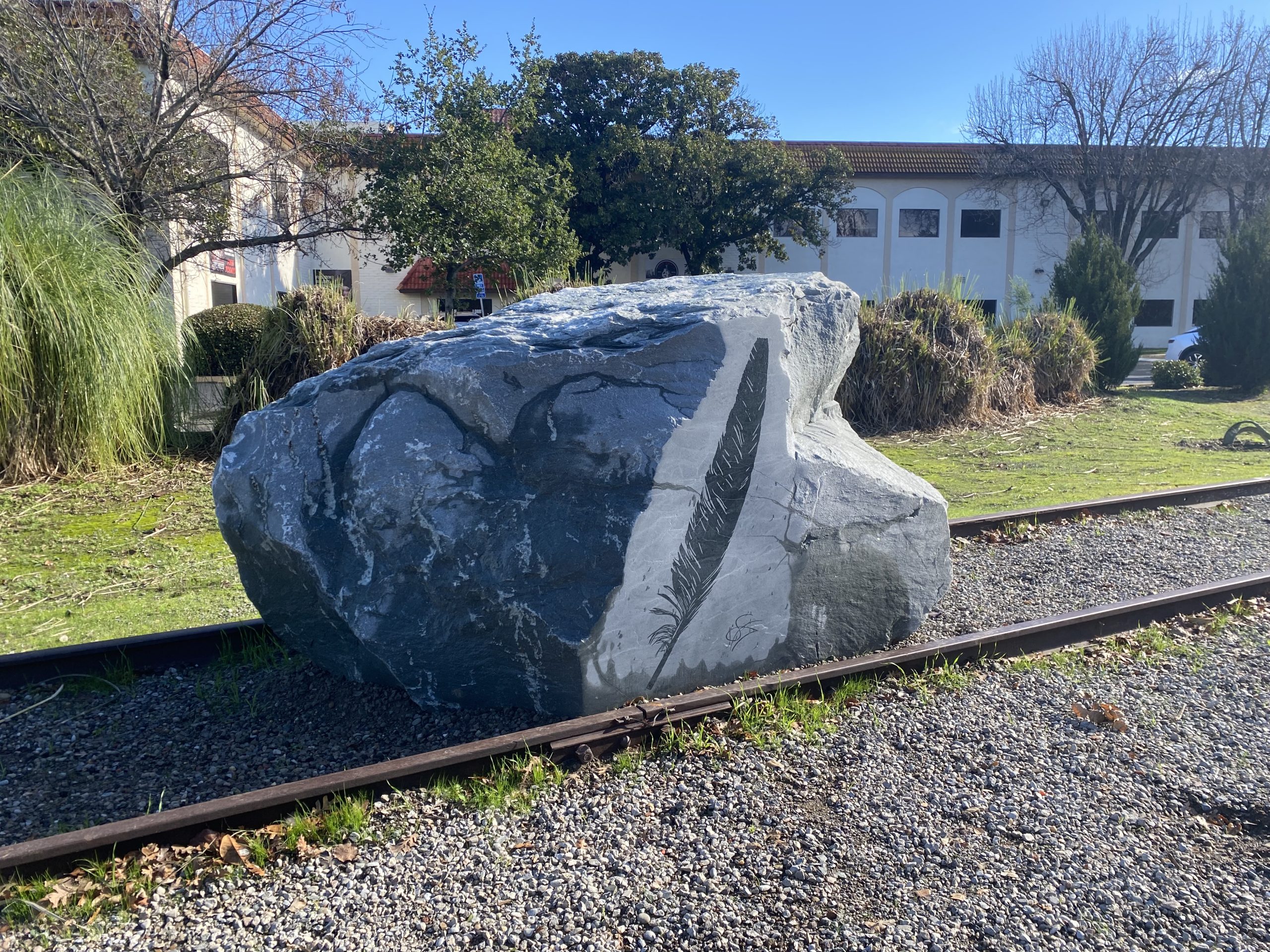 A boulder with a feather etched on the side sits on the railroad tracks.