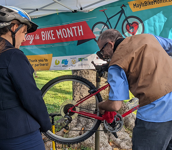 A man works on a bike while a woman wearing a bike helmet watches.