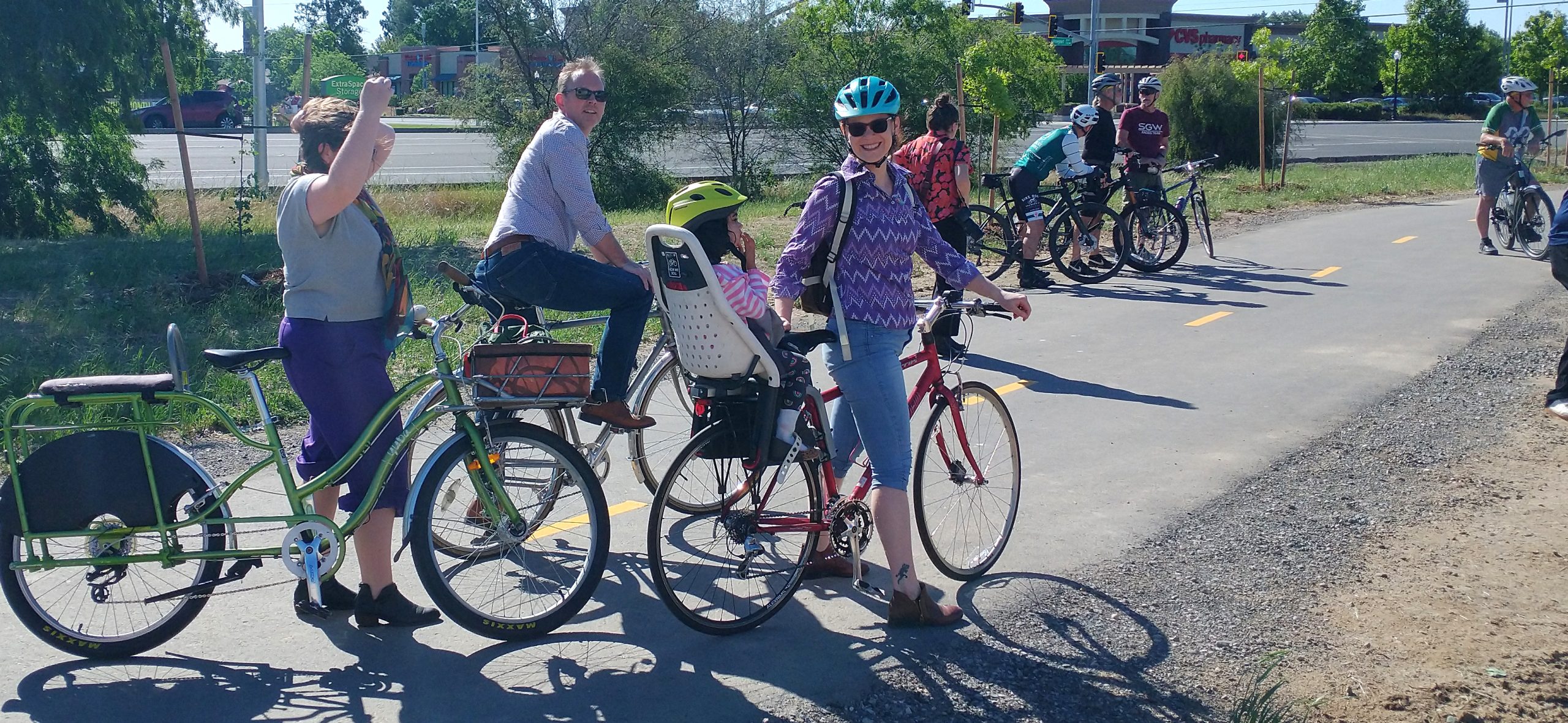 Several cyclists, one with a child on the back of their bike, on a bike path.