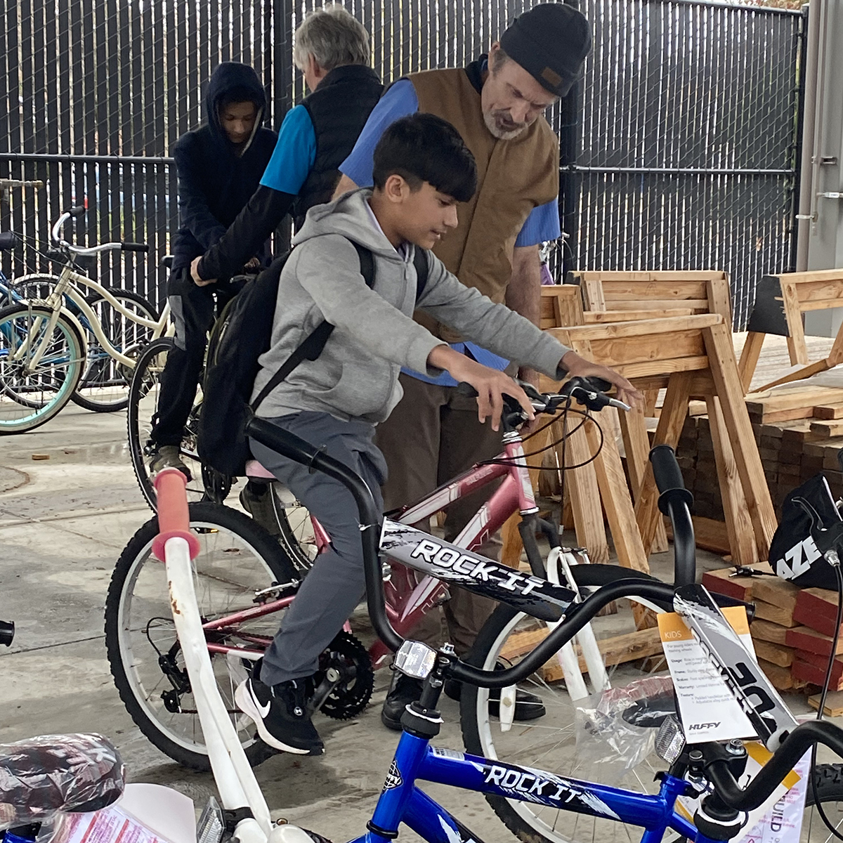 A man stands next to a boy who is trying out a bike.