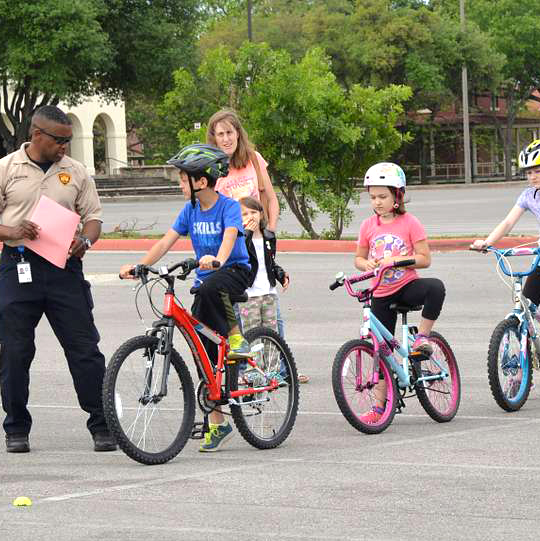 A man stands by 3 children on bikes in a parking lot.