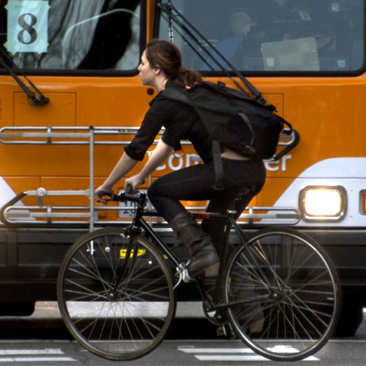 A woman rides her bike in front of a bus.