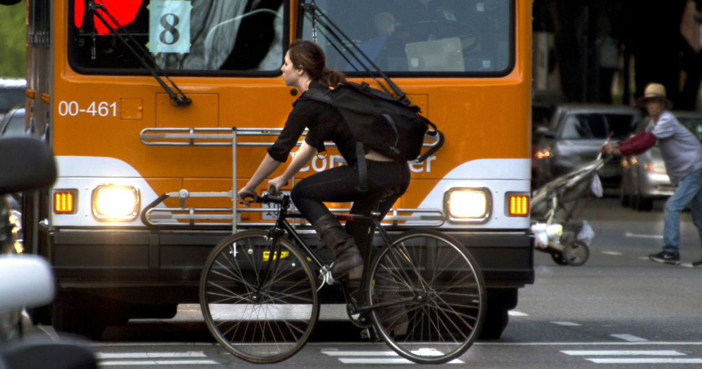 A woman rides her bike in front of a bus.