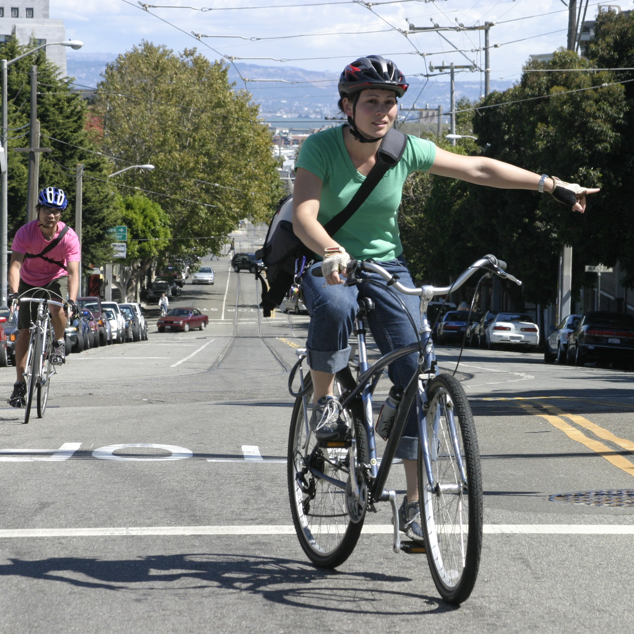 A woman riding a bike on a city street signals with her arm.