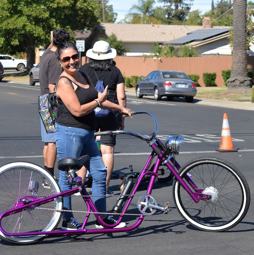 A woman stands next to a purple cruiser bike.