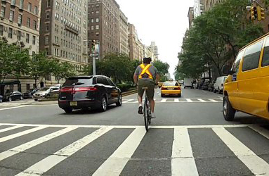 A cyclist rides down the middle of the street with cars on both sides.