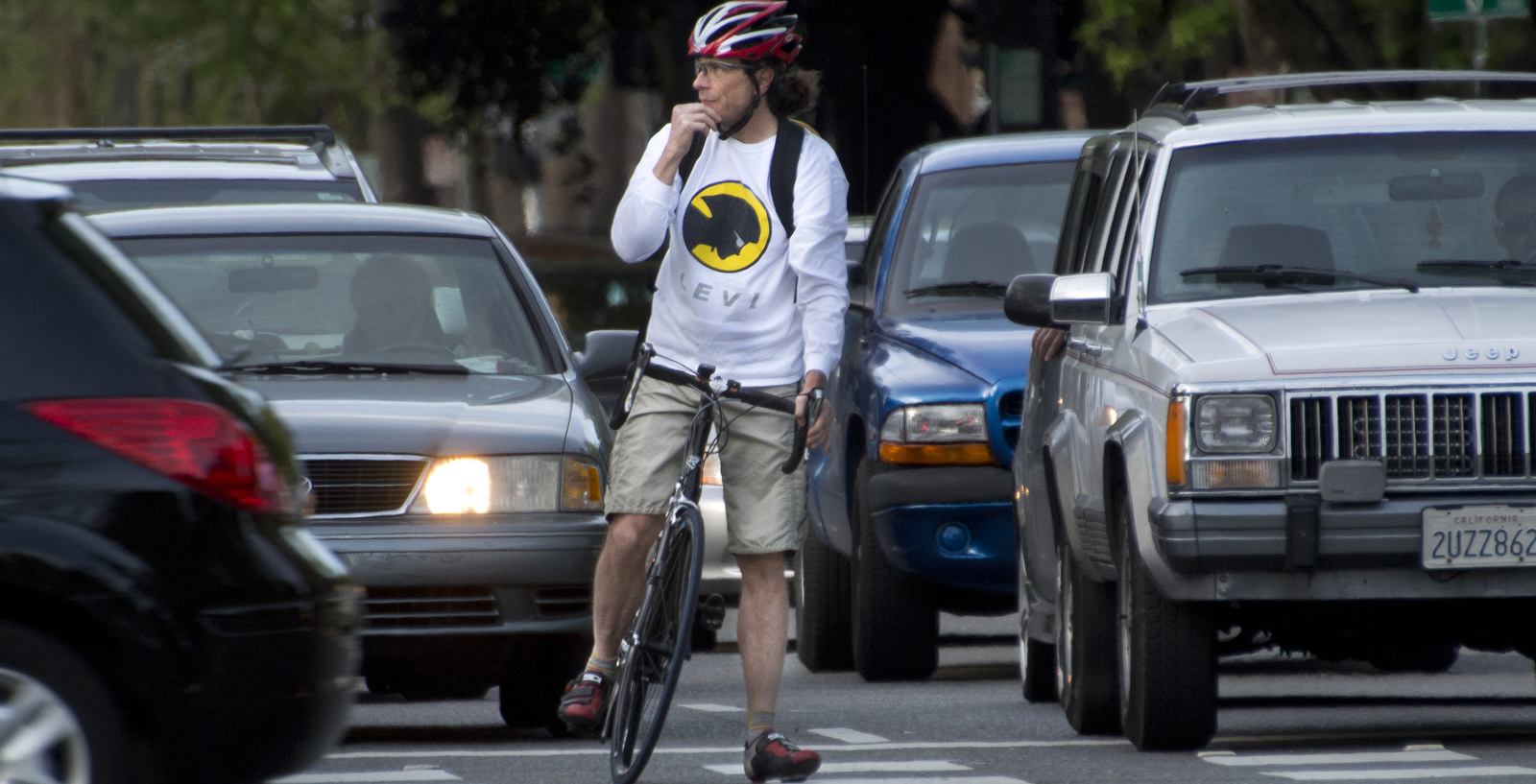 A man stopped on his bike between lanes of cars.