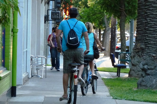 Two people ride their bikes on a sidewalk.