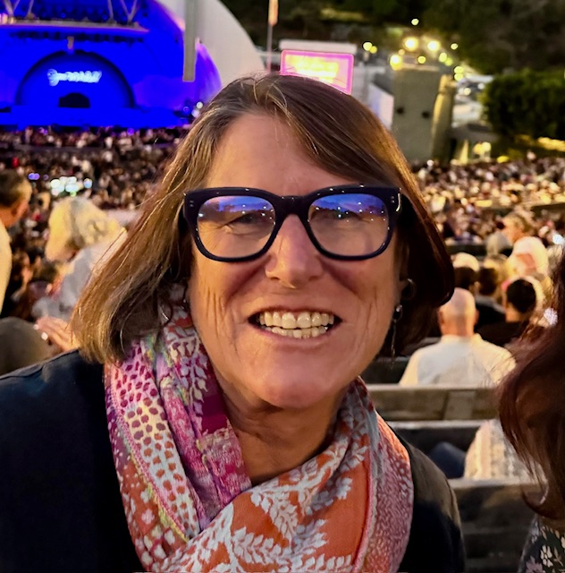 A woman wearing glasses and a red & white scarf smiles.