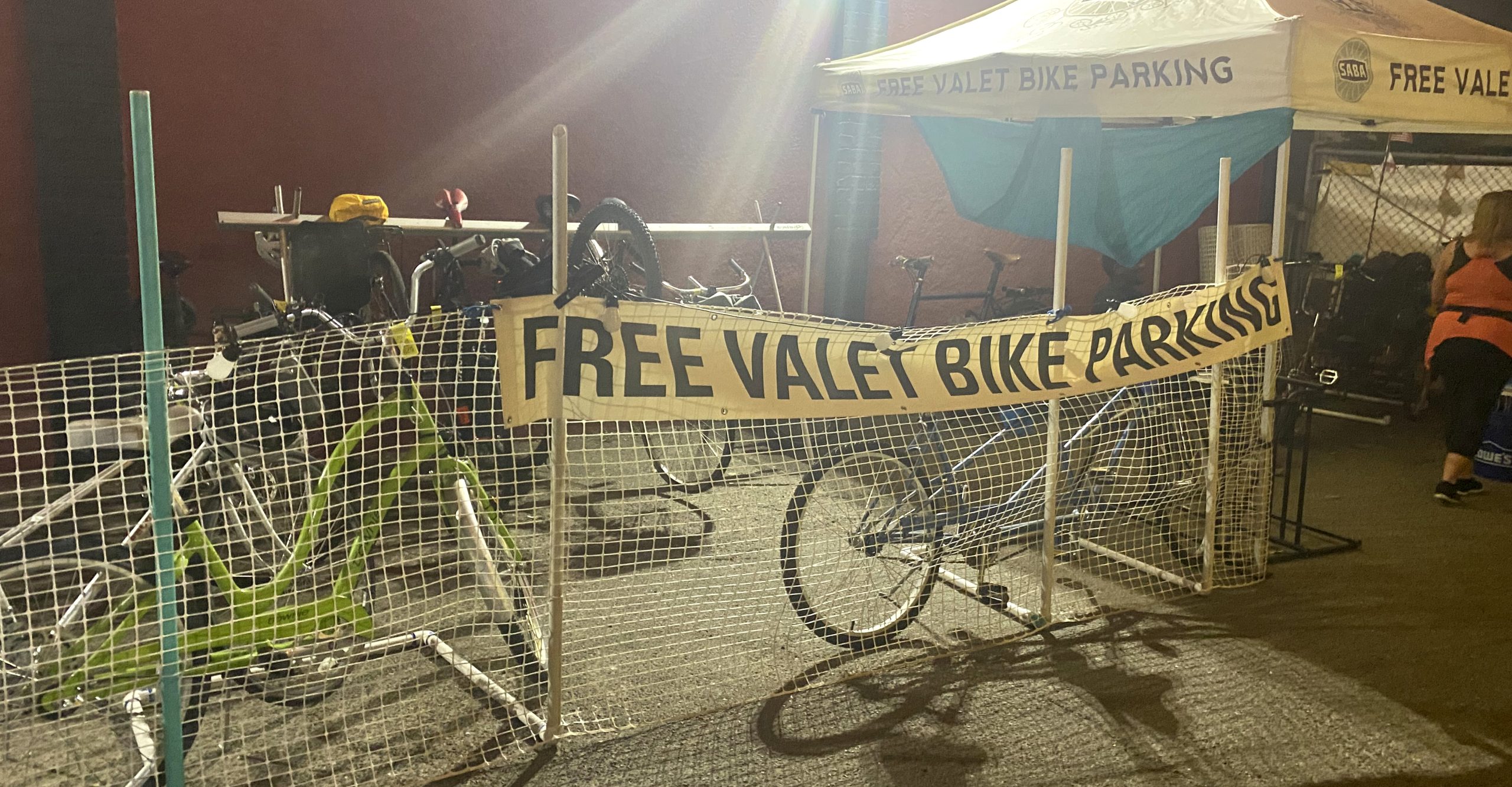 Bikes behind a wire fence with a banner that says, "Free Valet Bike Parking."