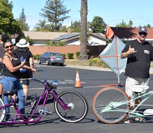 A woman stands next to a purple cruiser bike and a man stands next to a blue one.