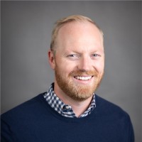 White man with reddish hair and beard wearing a dark blue sweater.