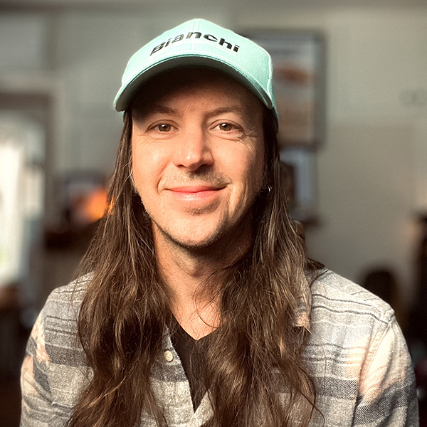 White man with long brown hair and a light blue cap.
